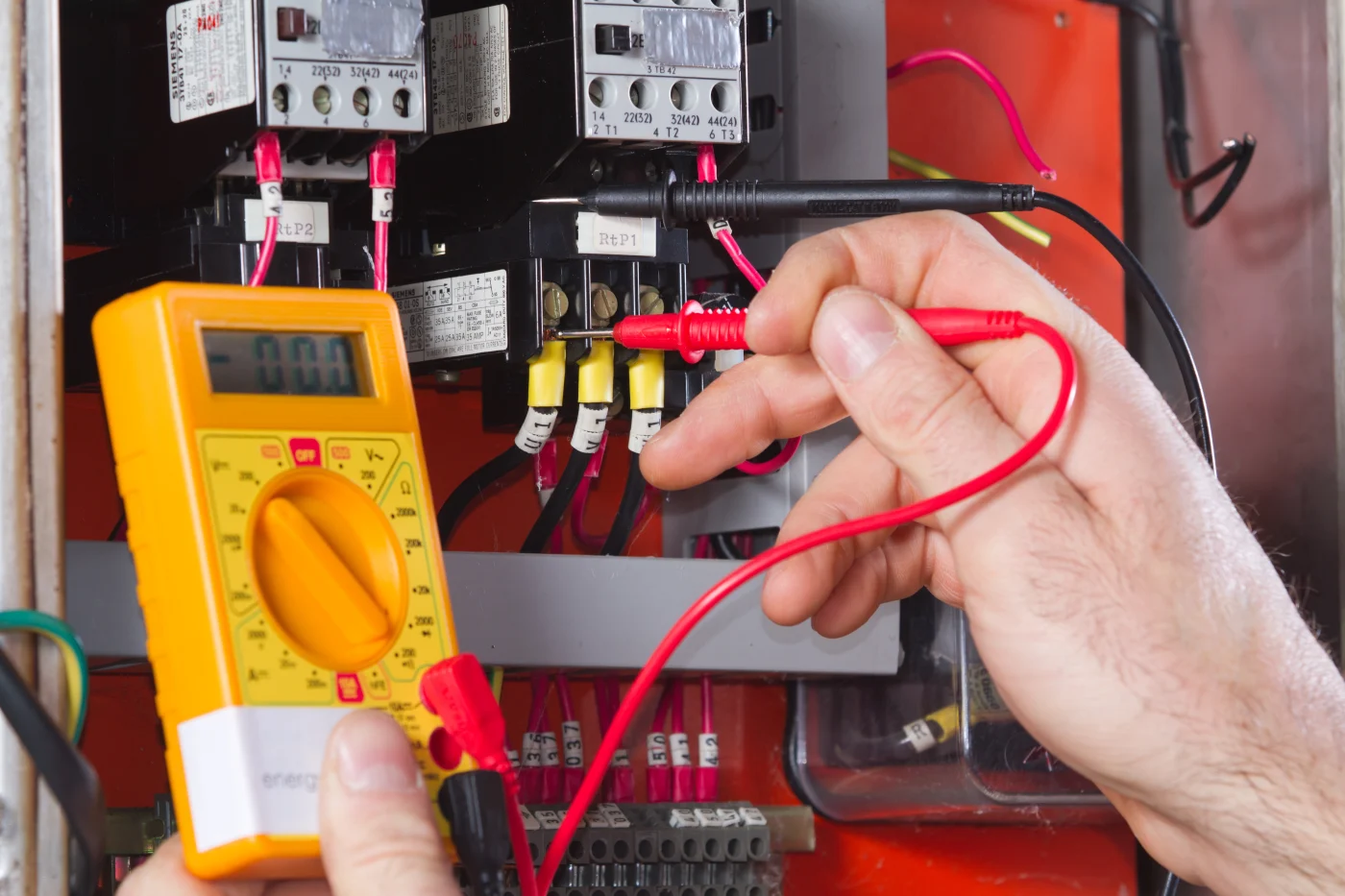 Electrician from Emerge Electric in Olympia, WA, is wearing a hard hat and protective gloves while checking a wall outlet with tester.