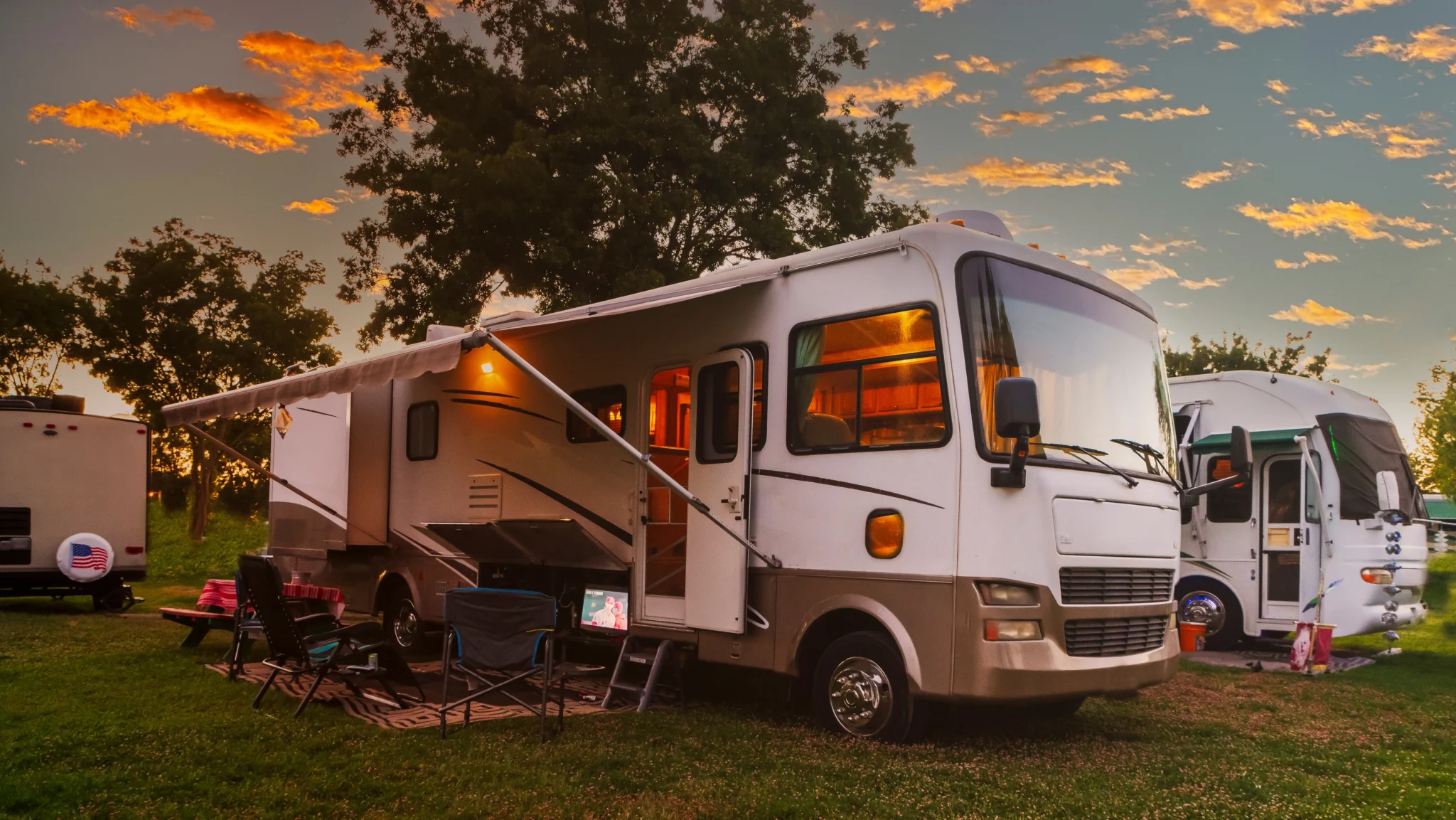 RV with lights on, awning out, and TV on with chairs