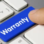 Close view of a computer keyboard with a finger poised above a big blue key inscribed with “Warranty” in white letters
